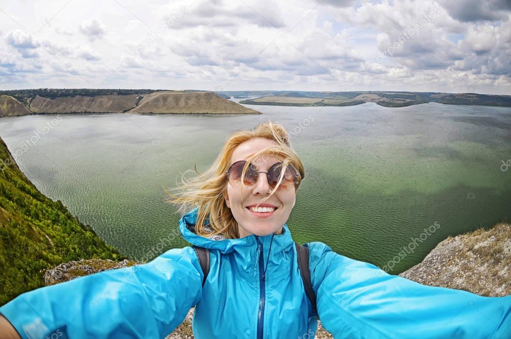 Smiling young woman takes a selfie  on mountain peak in Bakota 