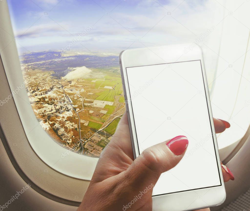Woman  sit near window , holding smart-phone working on board of airplane