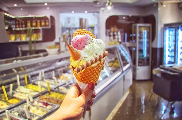 Italian ice - cream cone held in hand on the background of  shop  in Rome , Italy .It is one of the best ice cream place in town popular among tourists.