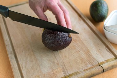 Avokadoyu bıçakla ikiye bölmek için eller tutuyor.