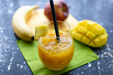 Lezzetli mango smoothie ile ezilmiş buz ve bardakta saman. Arka planda taze meyve. 