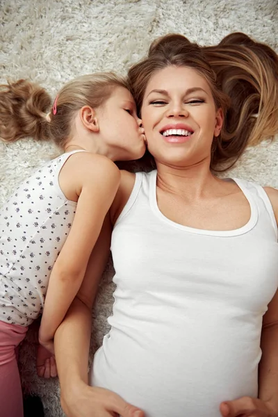 幸福的家庭躺在地板上 可爱的女孩亲吻她怀孕的母亲 — 图库照片