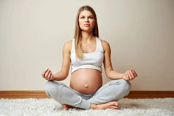 怀孕的女性冥想在瑜伽姿势坐在家里的地板上 图库照片