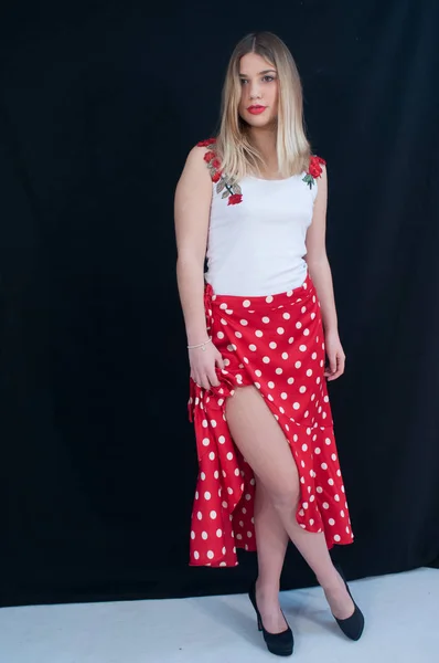 Schöne blonde Mädchen mit langen Haaren, mit roten Lippen, mit langem roten Rock und weißem Top mit floralen Motiven, Modefrau. einheitlicher schwarzer Hintergrund — Stockfoto