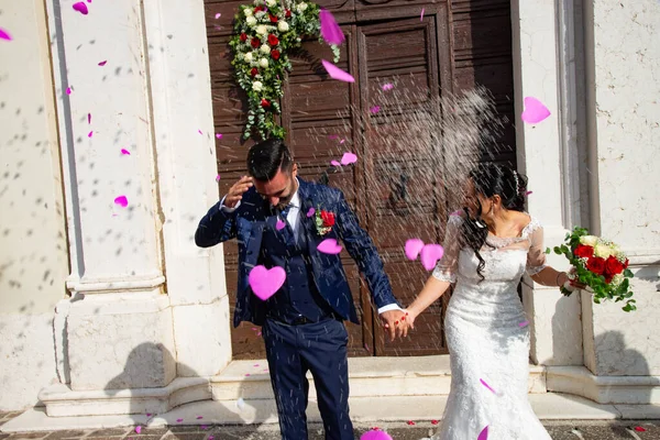 笑顔と幸せな若い夫婦は結婚後に教会を離れる ガルダ湖 トーリ ベナコ イタリア 結婚のための良い願いであるコンフェッティ コンフェッティと花の花びらの打ち上げ — ストック写真