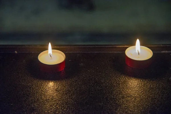 Close up of two votive candles in a church. Candles in the dark with flames on red copper supports.