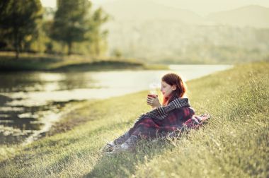 Sıcak çay içme Gölü sahilinde oturan kırmızı saçlı kız