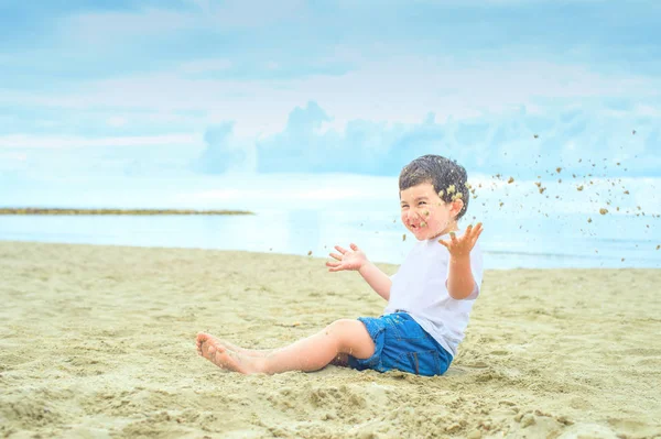 Bambino Felice Seduto Sulla Spiaggia Sabbia Gettando Sabbia Aria Ridendo — Foto Stock