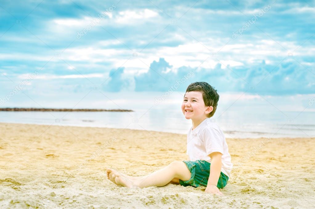 Cheeful child sitting on a sandy beach and laughing
