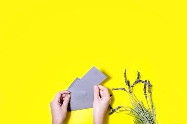 Üstten Görünüm eller gri zarf ve lavanta çiçekleri sarı arka plan üzerinde açma 