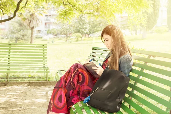 A beautiful young woman seated on a park bench spring — Stock Photo, Image