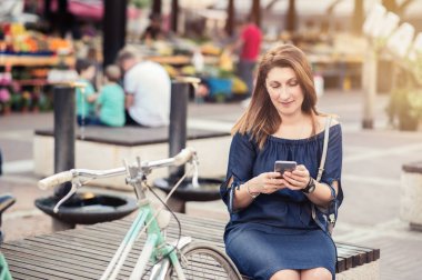 Bir şehirde bir bankta oturmuş bir akıllı telefon kullanan genç kadın