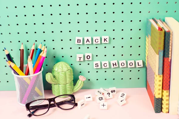 Voltar à escola fornece espaço de trabalho pastel com lápis, óculos, figura de cactos e letras de madeira em uma placa — Fotografia de Stock