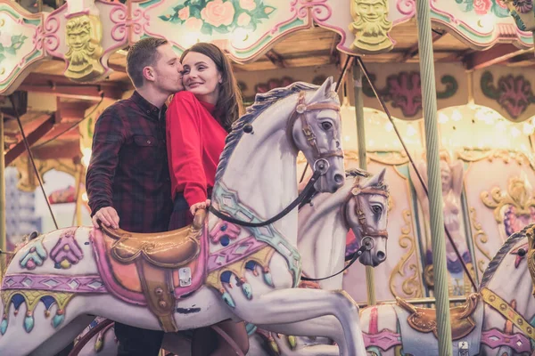 Romantische paar nemen een moment om te kussen terwijl het berijden van paarden op carrousel — Stockfoto