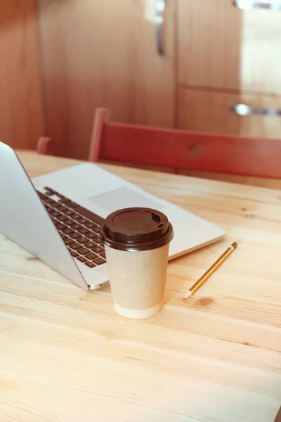 卡普奇诺拿铁在一个纸制纸杯上，桌上有笔记本电脑。 咖啡外卖去 — 图库照片