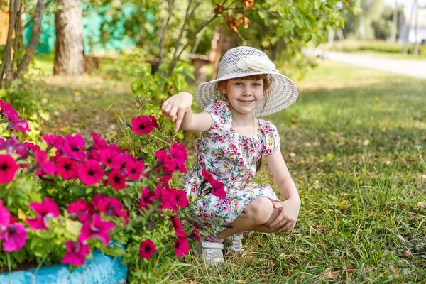 6-летняя девочка сидит рядом с цветами петуний — стоковое фото