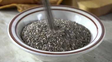 Yavaş çekimde küçük bir kaseye siyah chia tohumları dökülüyor.