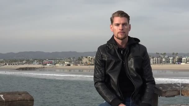 一位年轻貌美的男子正在渡假 坐在海面上的一个码头边 — 图库视频影像