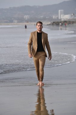 Havalı takım elbiseli yakışıklı bir adam sahilde yürüyor.