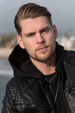 Plaj otelinde kapüşonlu ceketli yakışıklı bir genç.