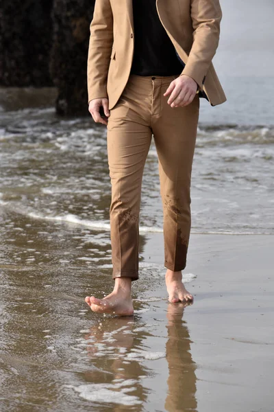 Feet of a man in a suit walking barefoot in the wet sand on the beach