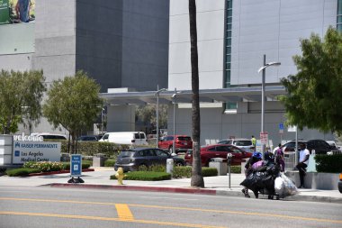 Los Angeles, CA/USA - May 4, 2020: A homeless man walks by as cars pull into a drive up COVID-19 testing area at Kaiser Permanante Hospital clipart