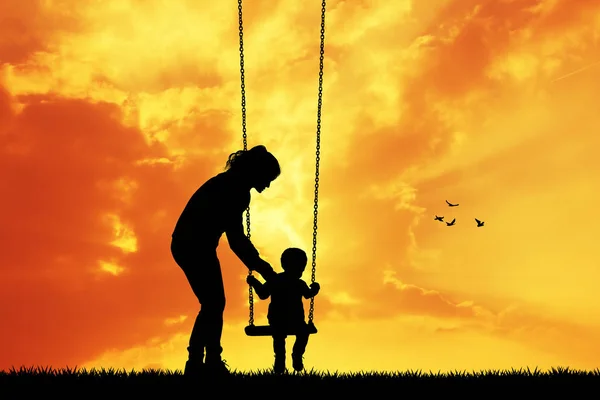 Mor och barn på swing på sunset — Stockfoto