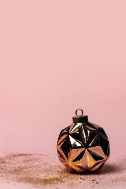 Modern geometrik altın Noel topu ve pembe arka planda parıltılar.
