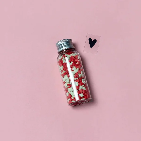 Butelka wypełniona cukierkami w kształcie serca i symbolem miłości na różowym tle. Miłość lub Walentynki koncepcja. — Zdjęcie stockowe