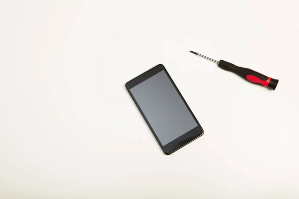 Смартфон и прецизионная отвертка поверх белого — стоковое фото