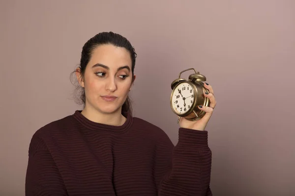 Jovem mulher olhando de forma duvidosa para um cloc alarme — Fotografia de Stock