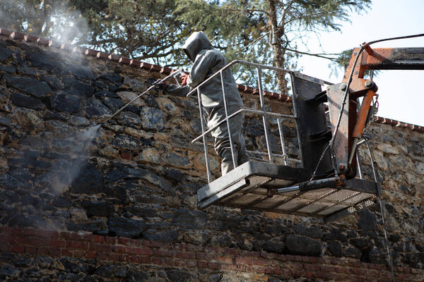 Man cleaning old dirty wall with high pressure water jet