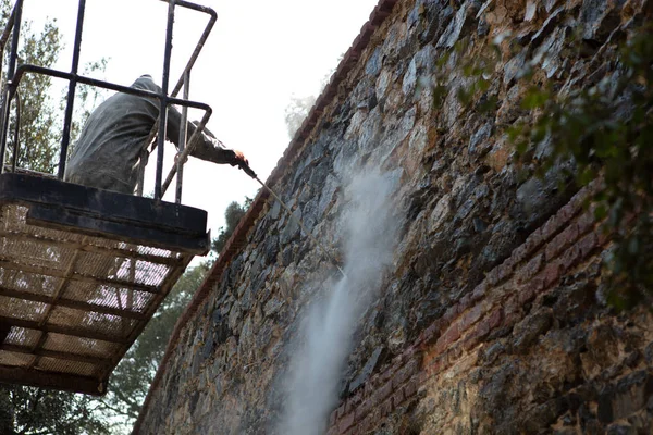 Werknemer is het sproeien van water voor de reiniging van de vuile muren Rechtenvrije Stockafbeeldingen