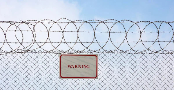 Warning sign hangs on a metal barbed wire fence ensuring safety and security.