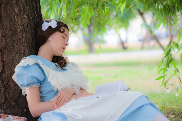 Niña alumna cayó sueño bajo un árbol con un libro . — Foto de Stock