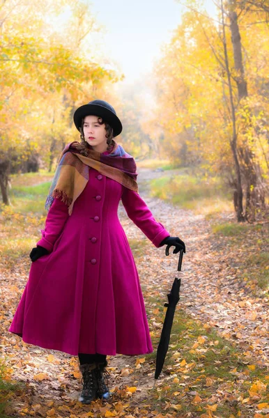 Ragazza in un luminoso cappotto cremisi a piedi nella foresta soleggiata giornata autunnale — Foto Stock