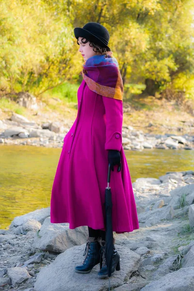 Chica con un abrigo carmesí brillante y un paraguas caminando por la rive —  Fotos de Stock