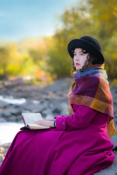 Menina ao ar livre em casaco brilhante está sentado e lendo livro — Fotografia de Stock