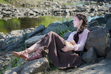 Genç kadın bir Boho tarzda nehir kıyısında kitap okuyor.