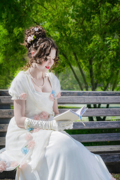 young happy woman is reading a book sitting on a bench.