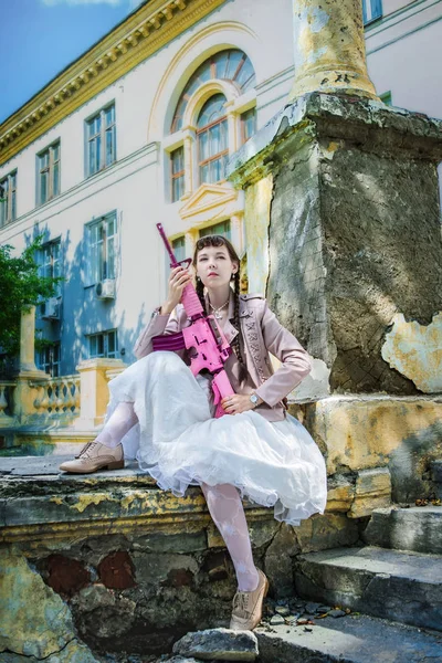 Ragazza in un abito bianco con un fucile rosa gioca airsoft — Foto Stock