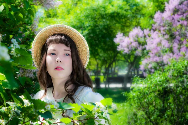 Niña en un vestido blanco y sombrero de paja cerca de flores de espino —  Fotos de Stock