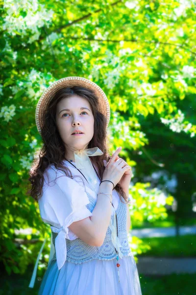 肖像画魅力的な女の子で白いドレスと藁帽子近く開花リンゴの木で公園 — ストック写真