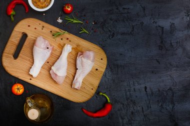 Koyu taş arka plan üzerinde yağ ve baharat ile bir kesme tahtası üzerinde Çiğ tavuk bacakları. Üst görünüm, düz döşeme, kopyalama alanı.