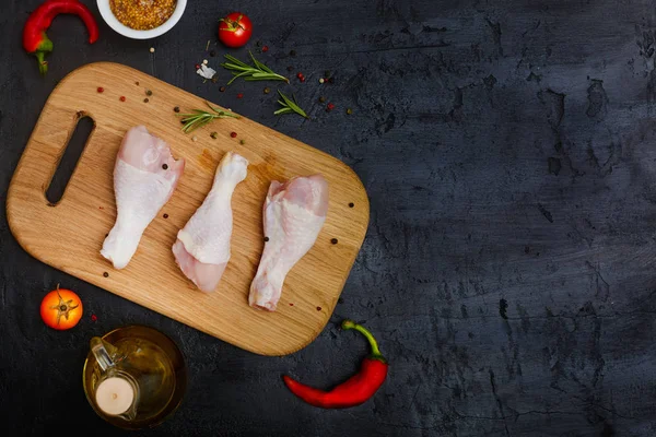 Koyu taş arka plan üzerinde yağ ve baharat ile bir kesme tahtası üzerinde Çiğ tavuk bacakları. Üst görünüm, düz döşeme, kopyalama alanı.