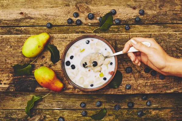 Eski bir rustik ahşap masada armut ve yaban mersini ile yulaf ezmesi bir kaşık ile kadın el. Üst görünüm, düz yatıyordu.
