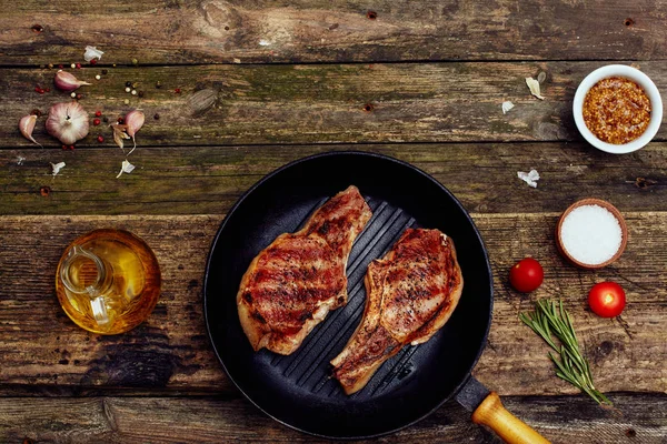 Eski ahşap bir masada çatal ve bıçak ile bir tabakta ızgara domuz pirzolası. Üst görünüm, düz yatıyordu. Kopyalama alanı