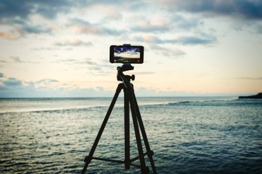 Seascape gündoğumu yakalayan tripod akıllı telefon. Mobil fotoğrafçılık veya videografi konsepti. 