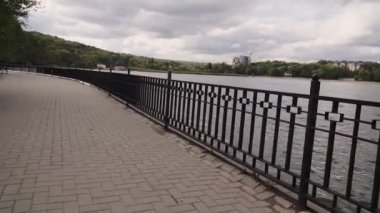 Şehir parkındaki boş bir göl kordonunun önünde kamera hareketi. Bulutlu sonbahar günü.