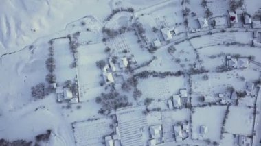 Kışın tarlalar ve ormanlar arasındaki hava manzaralı köy. Kış manzarası karla kaplı tarlalar ve kırsal kesimlerdeki ağaçlar.